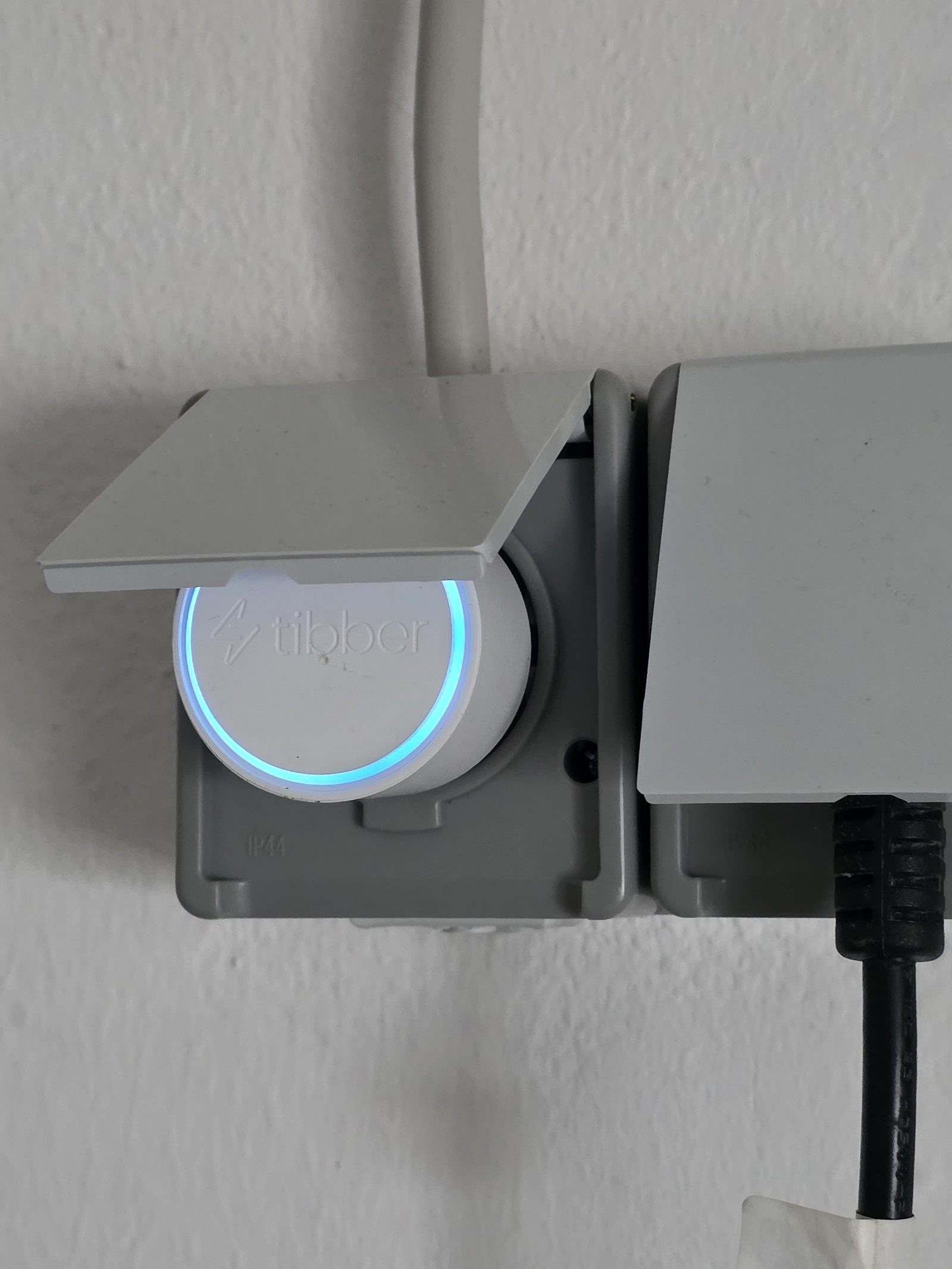 Tibber Pulse Bridge mit blau leuchtendem Ring in einer IP44-Außensteckdose